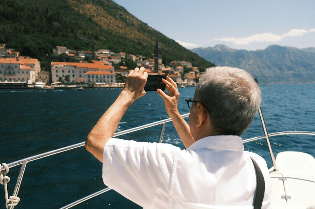Older man taking a photo of a mountain landscape with his smartphone
